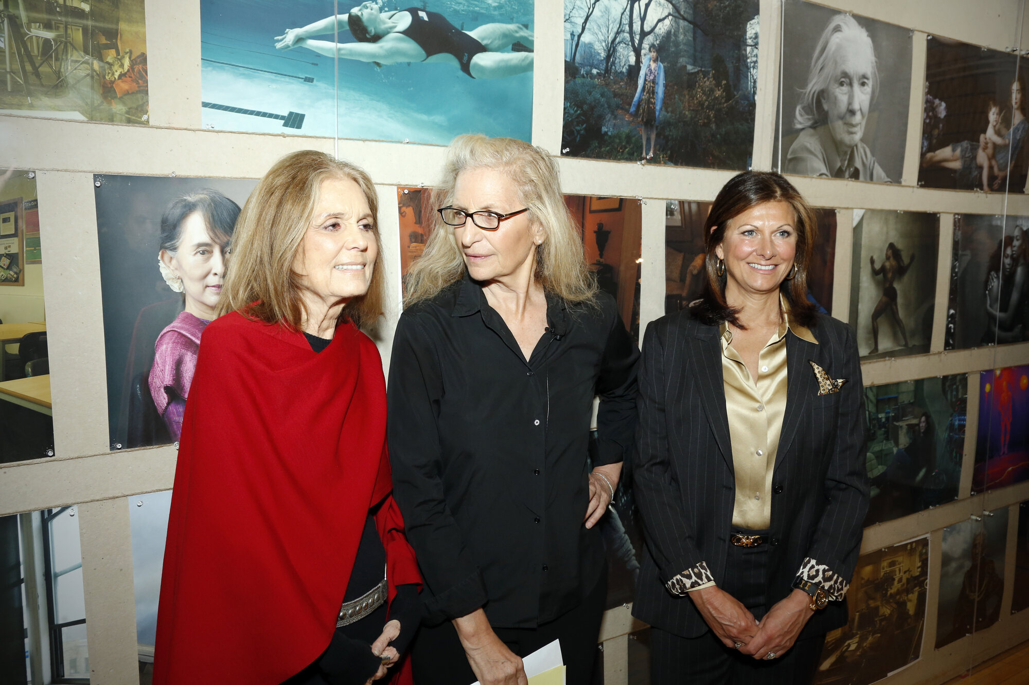 Gloria Steinem speaking at a Women for Women talk as Annie Leibovitz gestures toward the portrait wall