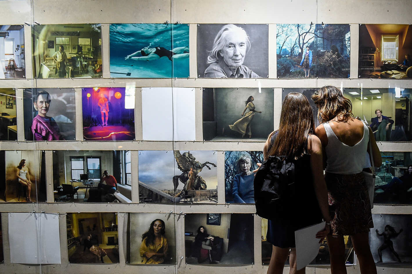 Two visitors viewing the full grid of portraits at the WOMEN exhibition